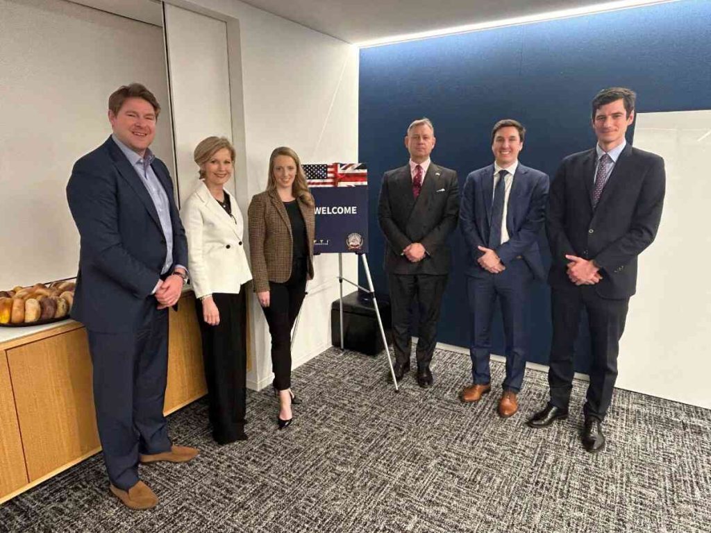 Two women and four men standing by welcome sign with British and American Flags