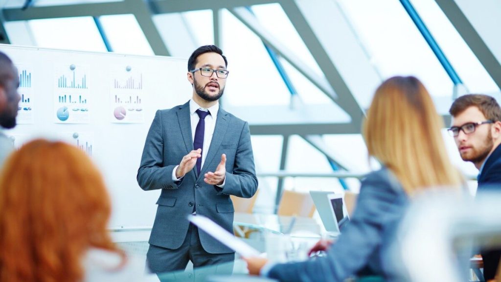 Man standing in front of whiteboard, talking to group of business people