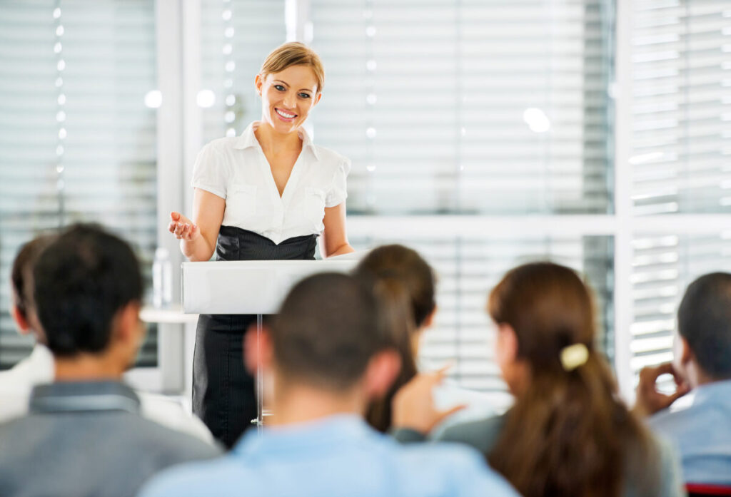 Women at podium in front of room with audience